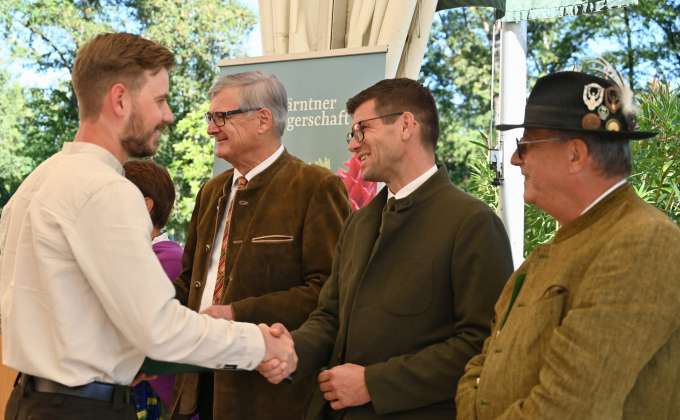 Gärtner gratulieren jungem Mann in Tracht bei Veranstaltung in Österreich.